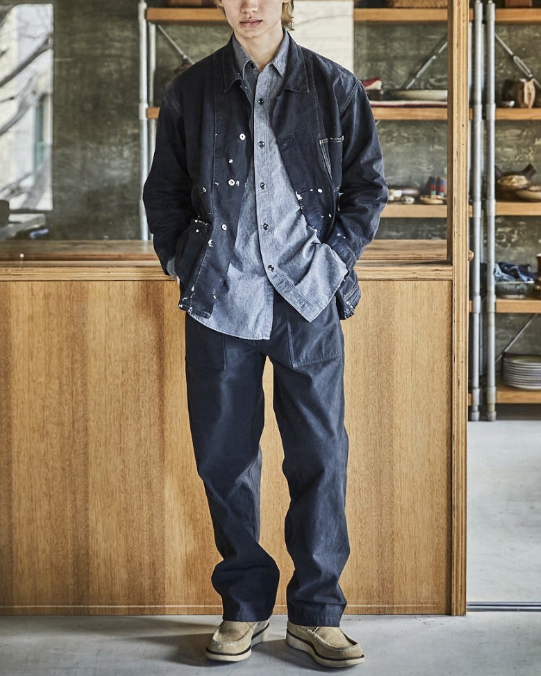 Homme portant une veste OrSlow Remade Herringbone Coverall noire avec projections de peinture chez Merci Paris