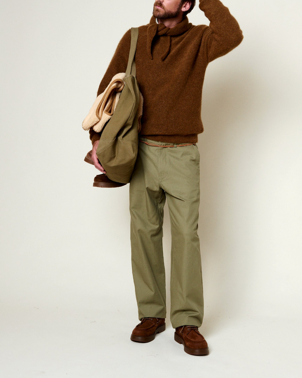 Homme portant un pull en alpaga marron Merci Paris avec un pantalon vert et un sac en toile sur fond clair