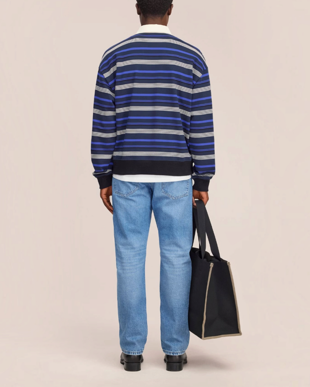 Vue arrière du polo rayé Merci Paris NN.07 en molleton de coton bleu, porté avec un jean et un sac fourre-tout noir.