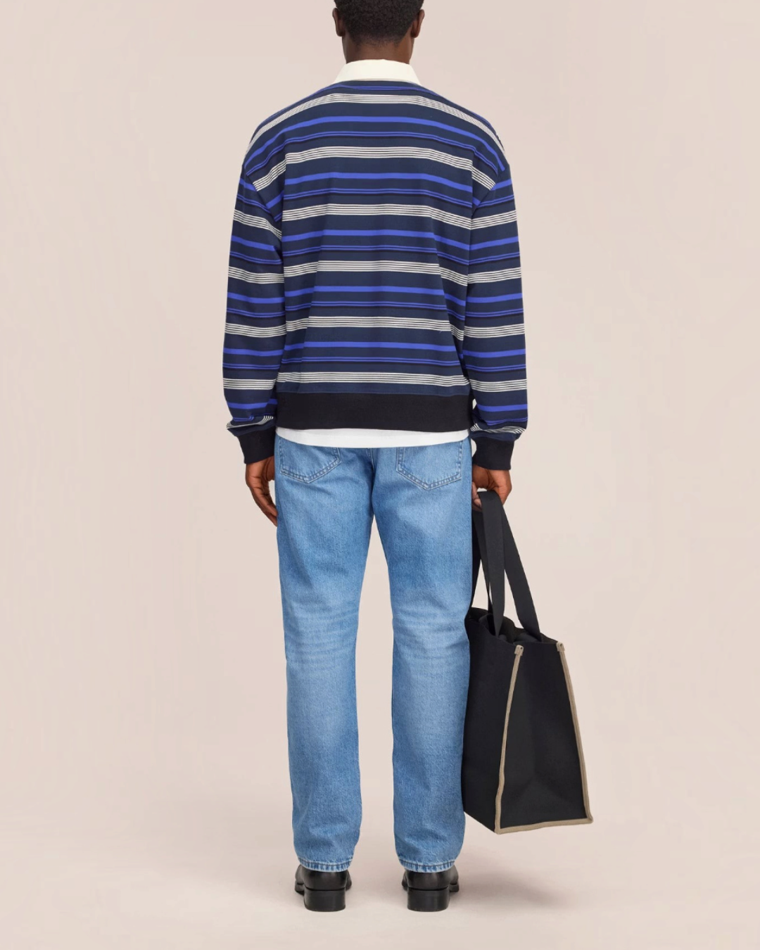 Vue arrière du polo rayé Merci Paris NN.07 en molleton de coton bleu, porté avec un jean et un sac fourre-tout noir.