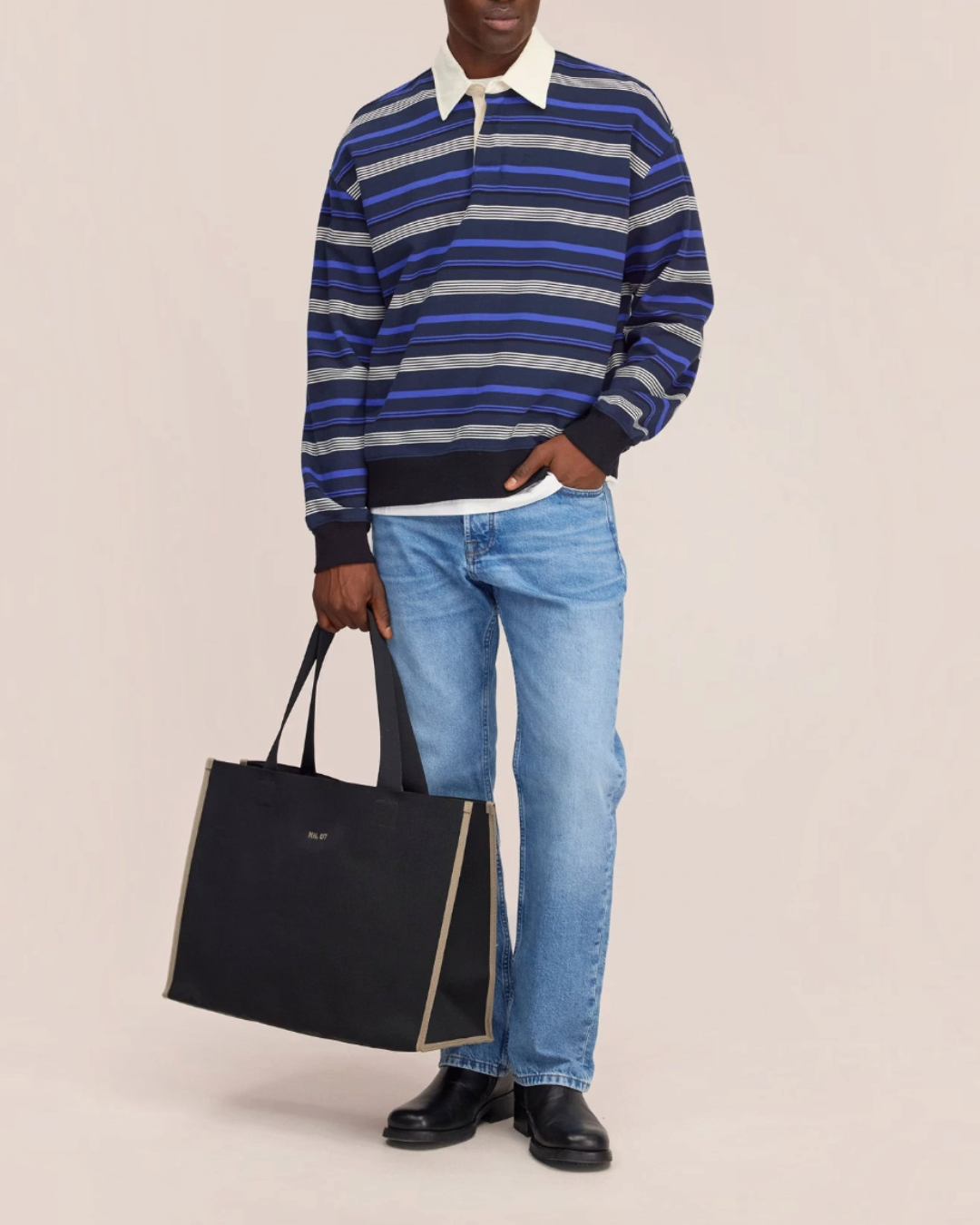 Homme portant le polo rayé bleu Merci Paris NN.07 à manches longues avec col contrastant et un grand sac fourre-tout