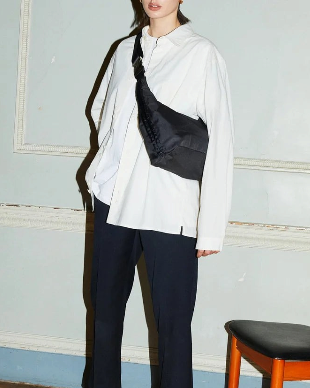 Merci Paris ARCS sac Petit Hey noir porté en bandoulière par une femme en chemise blanche dans un intérieur classique