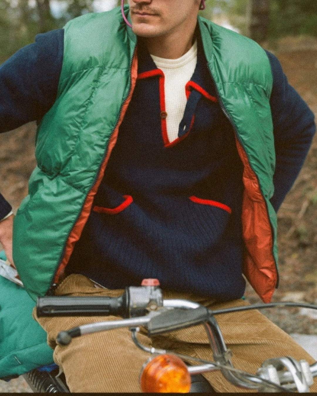 Homme portant une doudoune sans manches réversible Merci Paris Big Rock Candy verte sur un pull bleu en forêt