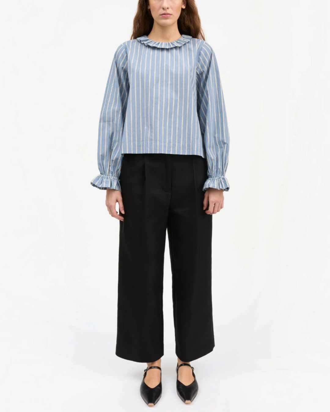 Modèle portant une blouse Skall Studio en coton biologique bleu à rayures, col rond volanté et manches bouffantes