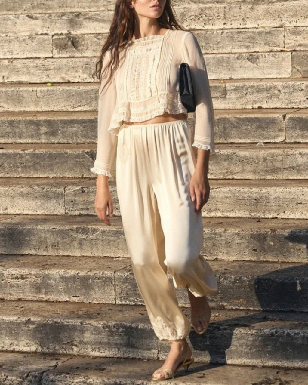 Model wearing the ecru Elodine blouse by Merci Paris in silk with lace and matching pants on steps