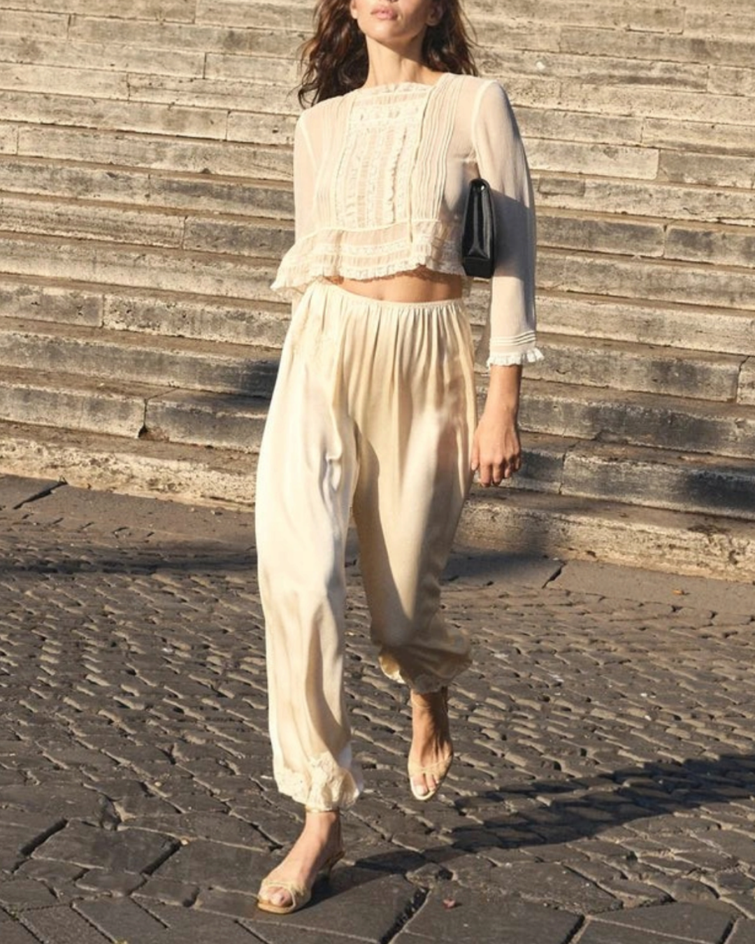Model wearing the short blouse Merci Paris Dôen Ecru silk elodine with lace and flared sleeves on steps