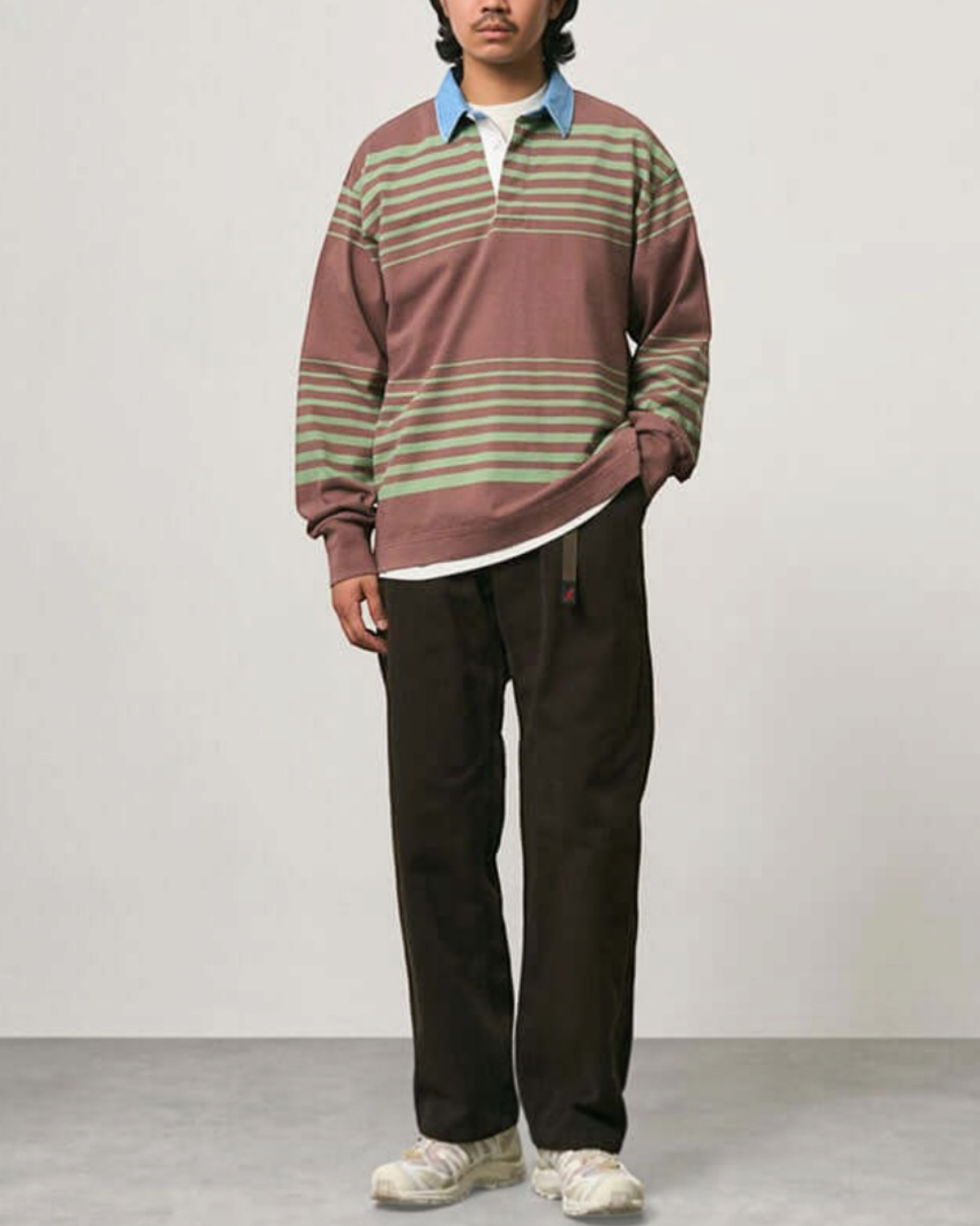 Homme portant un polo de rugby Gramicci à rayures marron et vert avec un col bleu contrastant chez Merci Paris