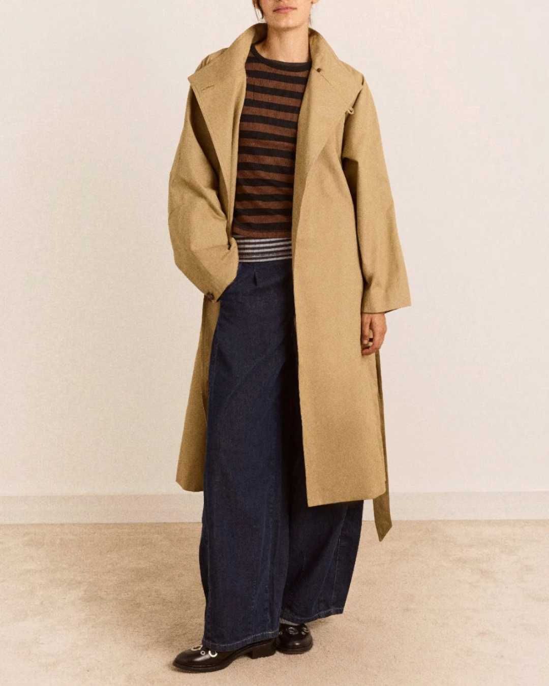 Trench beige mi-long Damson Madder en coton biologique avec col montant, porté par une femme sur fond neutre