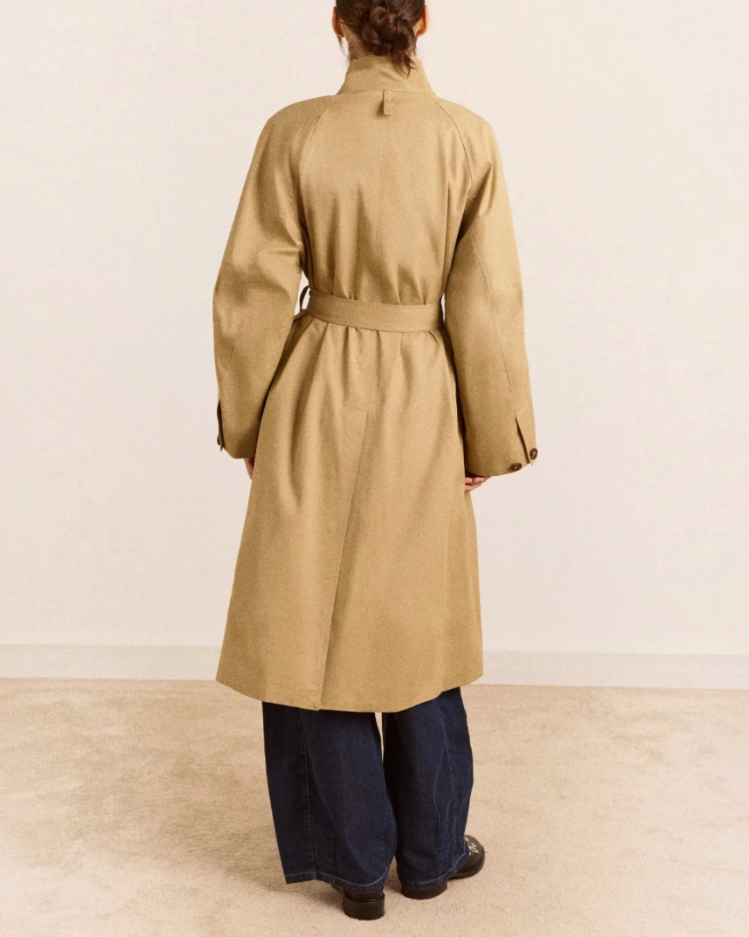 Vue arrière du trench beige Damson Madder en coton biologique avec ceinture et col montant, porté par une femme.