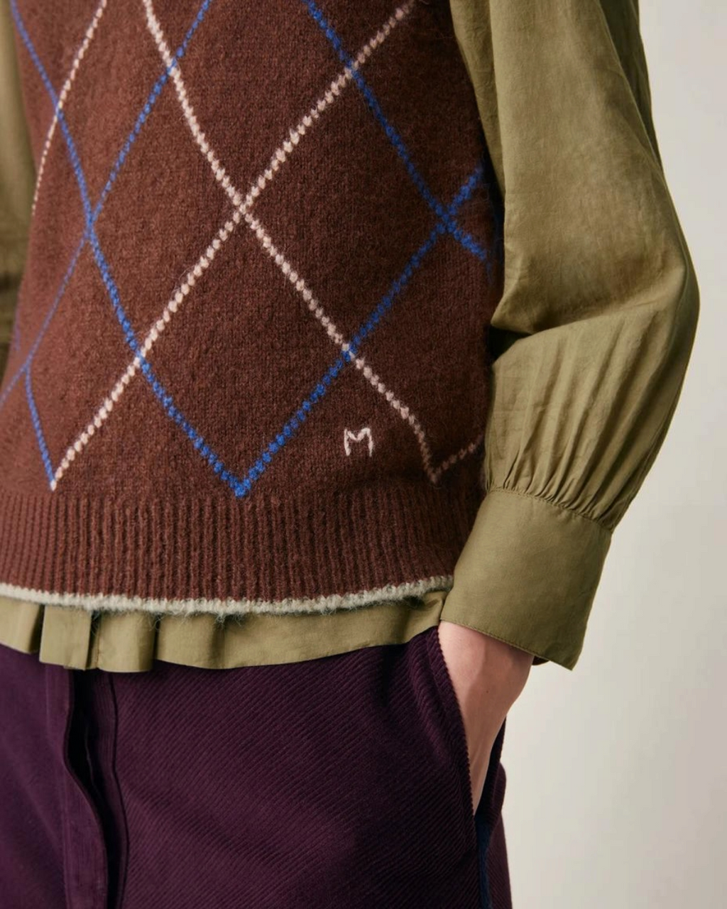 Pull sans manches Moismont Eddy en maille d'alpaga marron à motif losanges avec broderie M, porté sur une chemise