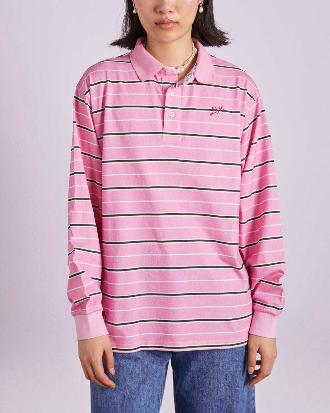 Modèle portant un polo Merci Paris Damson Madder à manches longues, rayures roses, noires et blanches en coton bio.