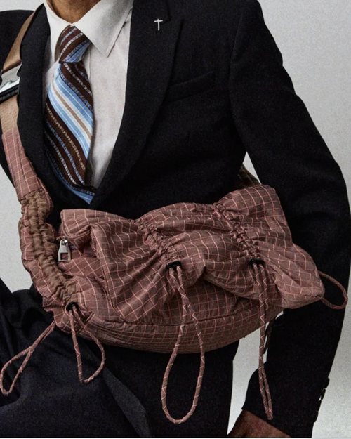 Homme en costume portant le sac modulable ARCS Sent en nylon rose à motif quadrillé, disponible chez Merci Paris