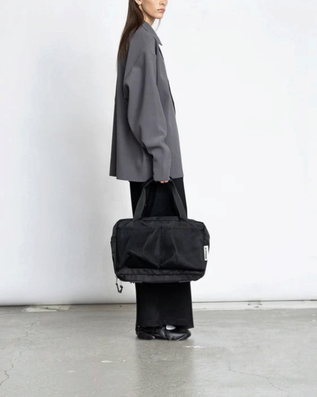 Merci Paris Ay Studios sac de voyage noir 18L en nylon recyclé porté par une femme sur fond blanc
