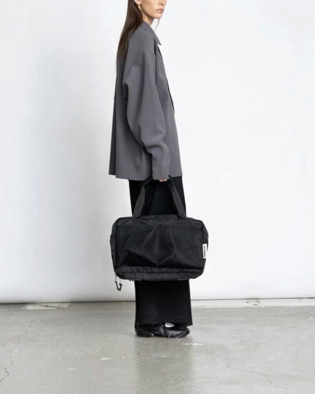 Merci Paris Ay Studios sac de voyage noir 18L en nylon recyclé porté par une femme sur fond blanc